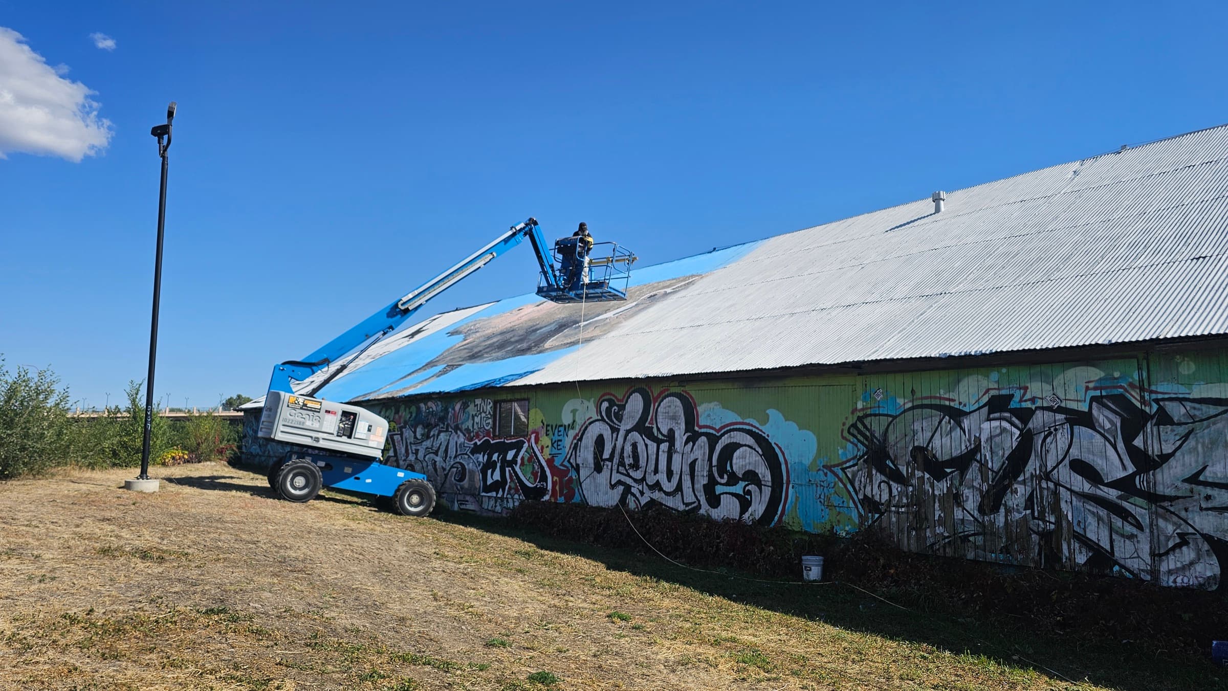 Worker on an elevated platform applying a coating to a large corrugated roof.