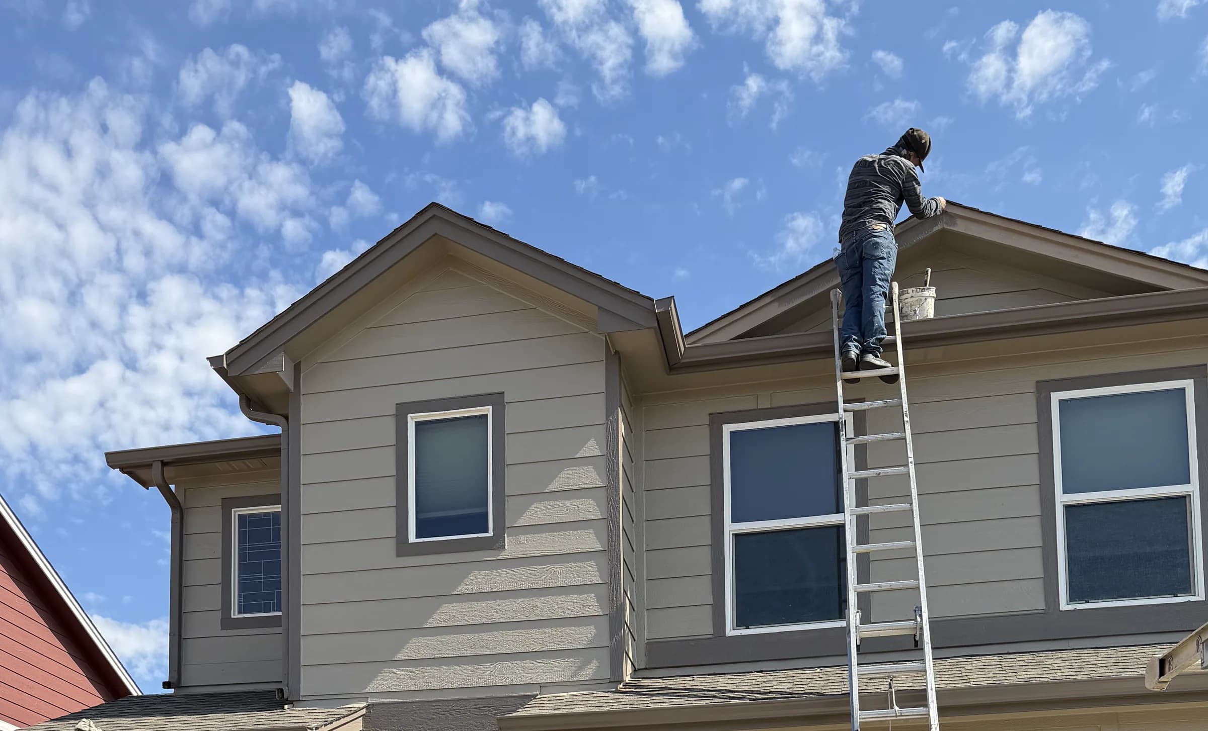 Gardiner painter working from a ladder along an upper residential roofline
