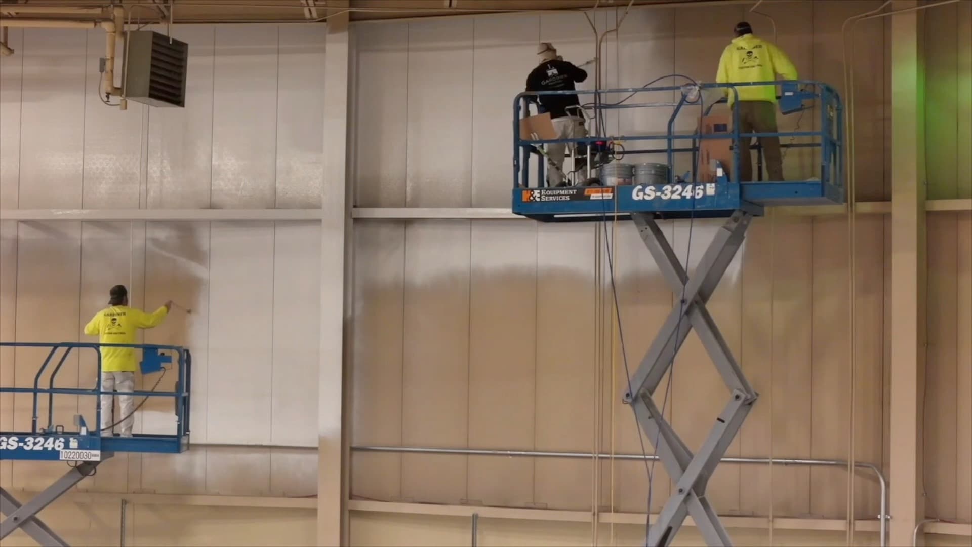 Three workers painting a large interior wall from elevated work platforms.